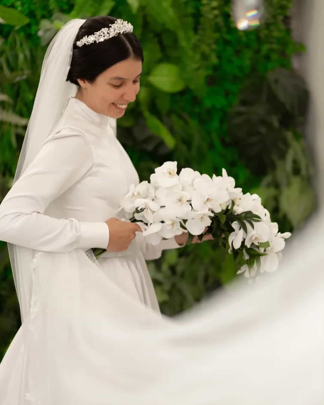 Noiva belíssima com buquê de Orquídeas Brancas em formato cascata com folhagem e fita decorativa, ideal para casamento religioso.