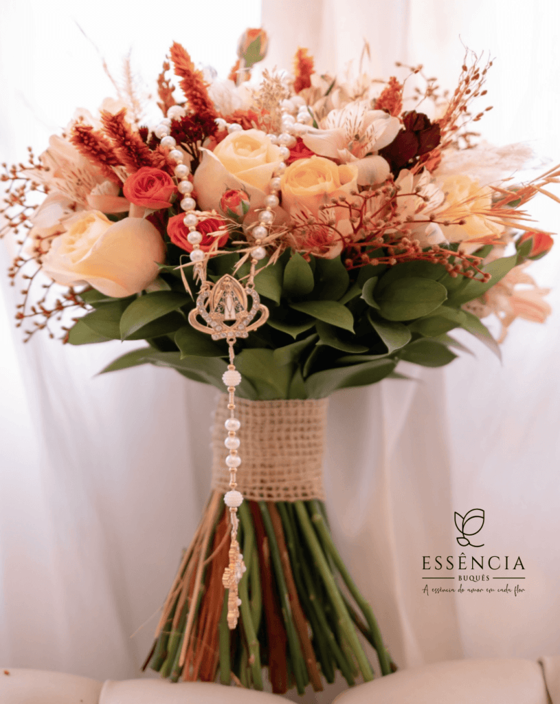 Buquê colorido, desconstruído com tons rosa e laranja claros, vermelho com folhagem e fita decorativa, ideal para casamento religioso.